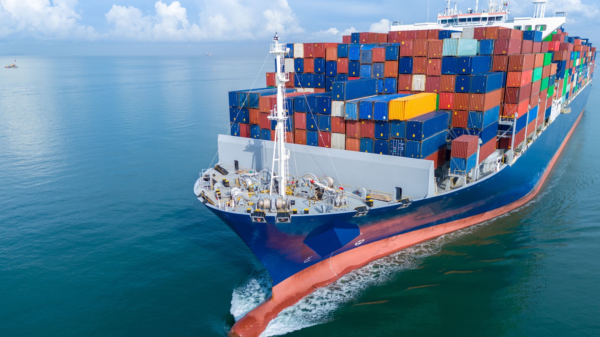 Aerial front view of a large cargo ship fully loaded with colorful shipping containers navigating through calm ocean water. Ideal for logistics, transport, and global trade concepts.